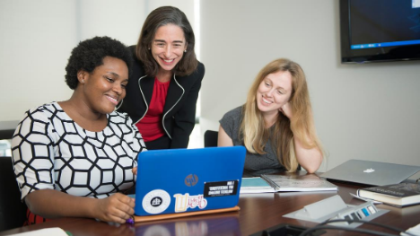 An instructor working with two students at a laptop.